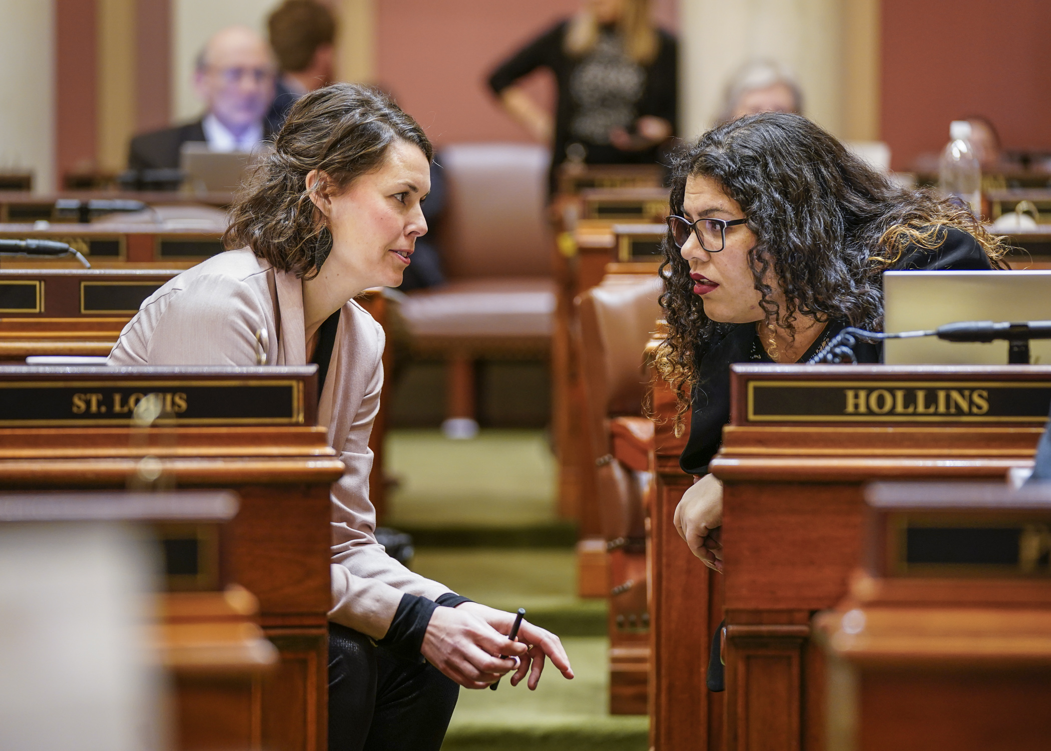 Rep. Liz Olson, left, talks with Rep. Athena Hollis during debate on the House Floor Feb. 16. (Photo by Catherine Davis)